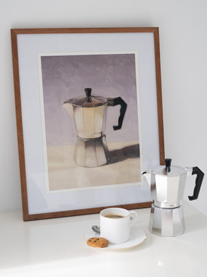 Framed artwork of a coffee Moka pot next to a real Moka pot and a cup on a white surface.