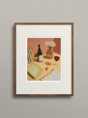 Framed artwork of a still life scene with books, wine bottle, and glass on a table.