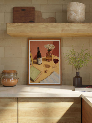 Framed artwork on a kitchen counter with a bottle, book, and wine glass illustration.