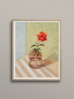 Framed artwork of a red rose in a glass vase on a striped surface with a gray background