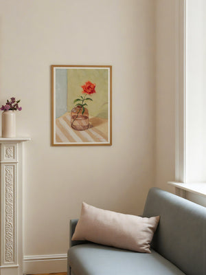 Framed artwork of a red flower in a glass vase on a wall above a sofa with a pillow.