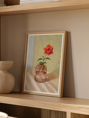 Framed painting of a red flower in a glass vase on a wooden shelf.