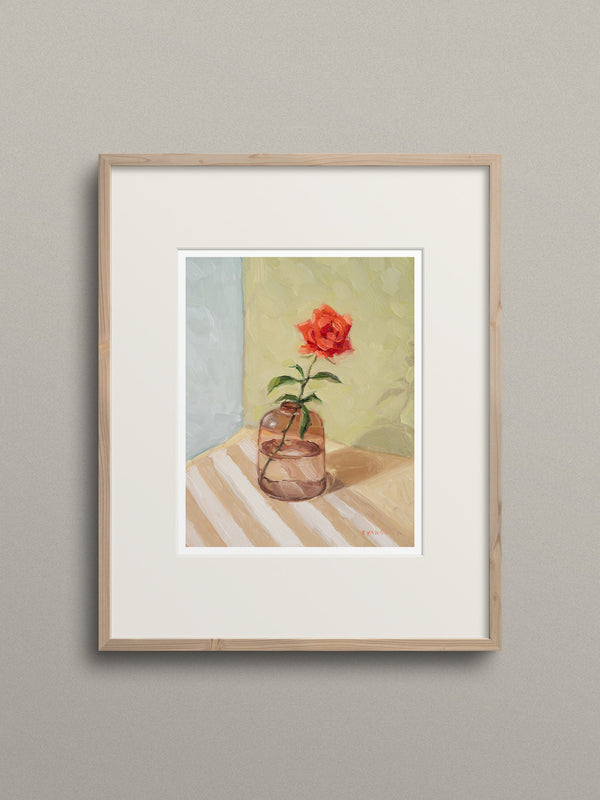 Framed artwork of a red flower in a glass vase on a striped surface.
