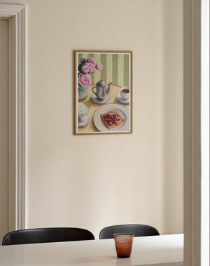 Framed art print featuring a table setting with a silver coffee pot, cup, whipped cream, crepe with strawberries, and flowers, hanging on a wall in the dining room